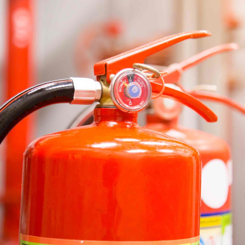 Close-up of a red fire extinguisher with a pressure gauge and black hose.