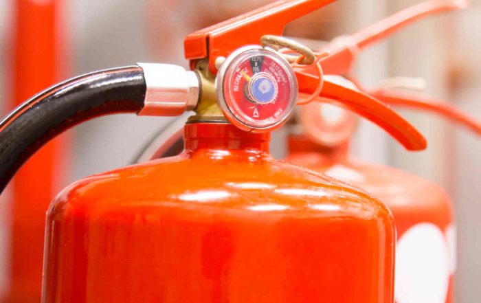 Close-up of a red fire extinguisher with a pressure gauge and black hose.