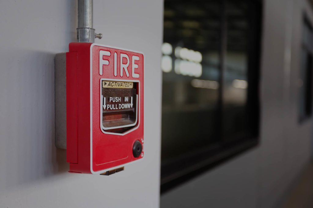 Red fire alarm on a wall with a "Push in, Pull Down" instruction. Blurred background.