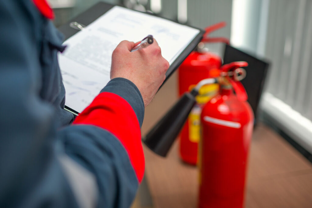 Fire Extinguisher Service Person in safety gear holding a clipboard, inspecting fire extinguishers.