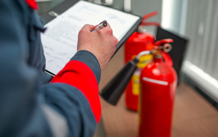 Fire Extinguisher Service Person in safety gear holding a clipboard, inspecting fire extinguishers.