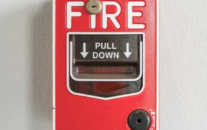 A red fire alarm box on a white wall displays instructions to "Pull Down" in case of emergency. Regular fire alarm inspections ensure its reliability when needed most.