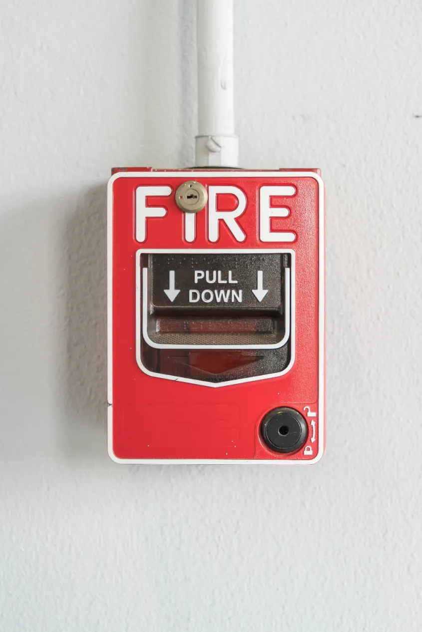 A red fire alarm box on a white wall displays instructions to "Pull Down" in case of emergency. Regular fire alarm inspections ensure its reliability when needed most.