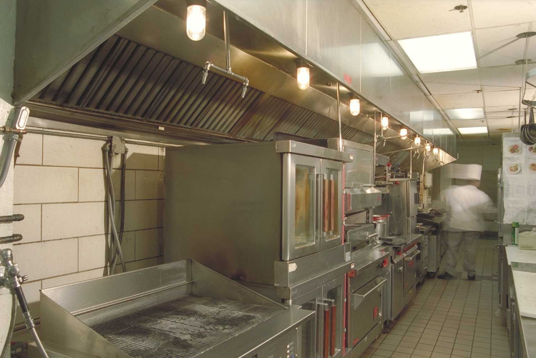A commercial kitchen with stainless steel appliances and a chef working near the back.