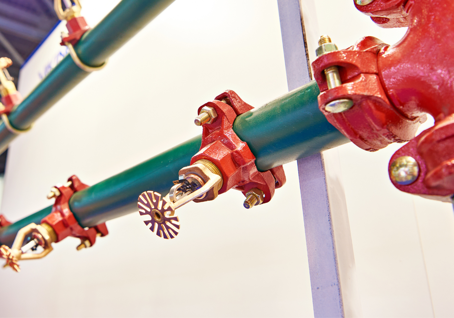 Close-up of a green pipe with red fittings and a fire sprinkler head attached, indoors.